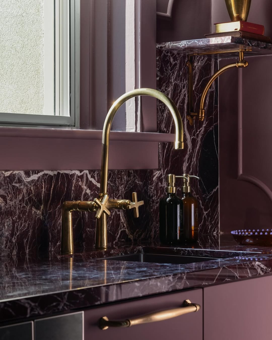 Unlacquered brass bridge kitchen faucet installed over farmhouse apron sink